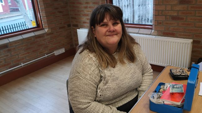 A photo of a woman sitting in front of an open cash box with money in it.