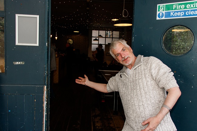 Mark gesturing for you to come inside a building